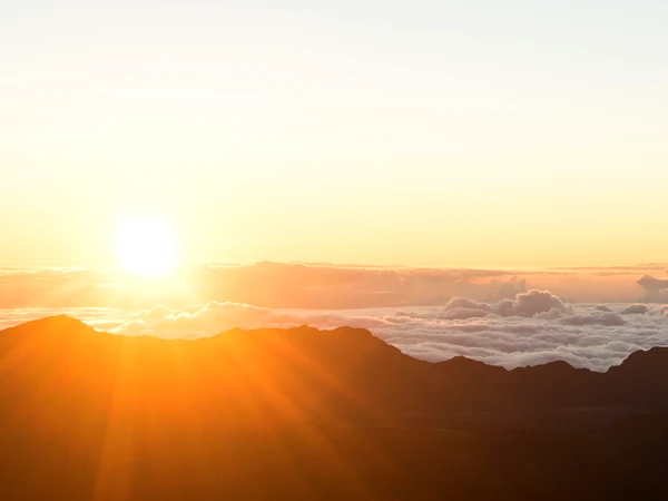 The sun rising over the mountains above a sea of clouds